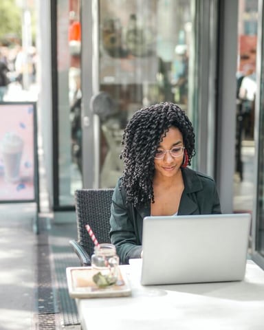 Woman working on laptop at outdoor café table on busy city street