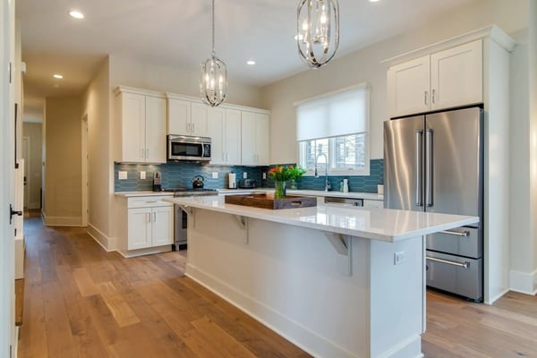 Modern kitchen with white cabinetry, stainless steel appliances, blue subway tile backsplash, white quartz island, and hardwood floors.