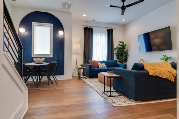 Open-plan living room with blue sectional sofa, wall-mounted TV, and navy accent nook with desk and mirror