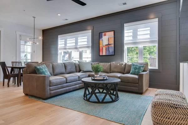 Open-plan living room with brown leather sectional sofa, round black coffee table, and large windows overlooking trees