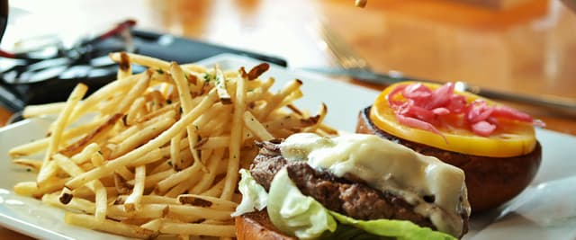 Cheeseburger with lettuce and melted cheese, served with crispy fries and a red-topped appetizer on white plate