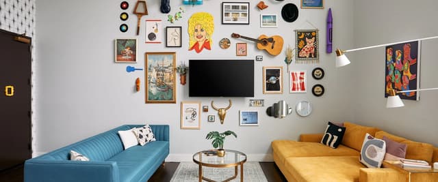 Living room with blue and yellow sofas, gallery wall of eclectic art and vintage objects, flat-screen TV, and round coffee table.