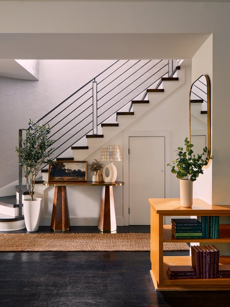 Modern entryway with floating wooden staircase, metal cable railing, console table with plants, and wood shelving unit.