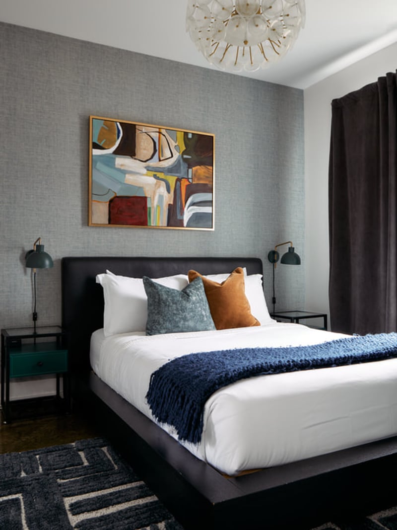 Modern bedroom with black bed, gray textured walls, abstract artwork, pendant light, and dark curtains