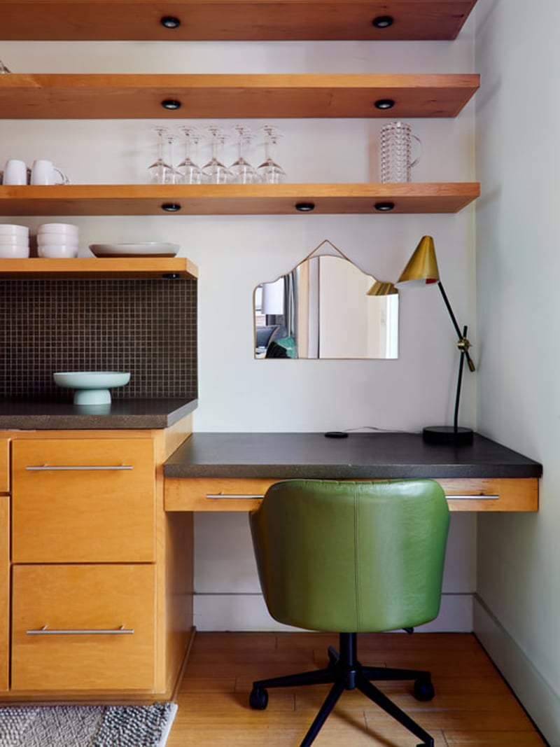 Home office nook with wooden desk, green chair, floating wood shelves, and brass desk lamp