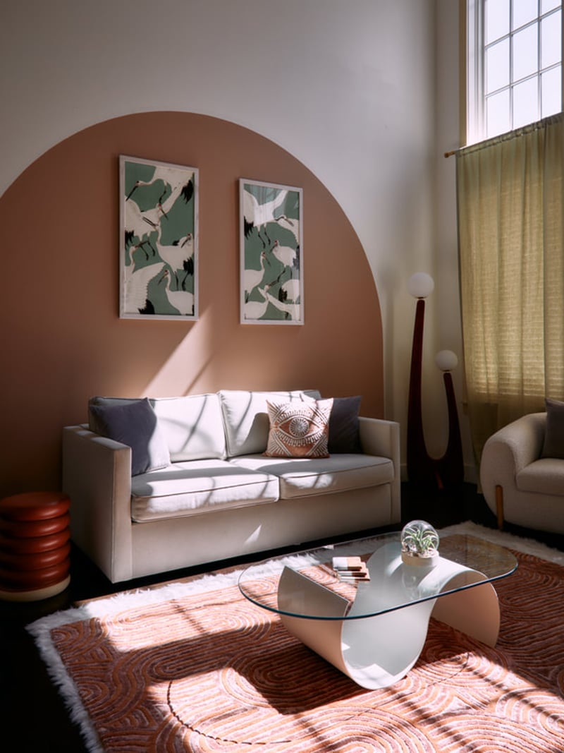 Modern living room with terracotta accent wall, cream sofa, glass coffee table, and botanical wall art