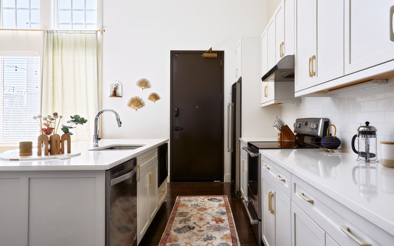 Modern galley kitchen with white cabinetry, white countertops, stainless steel appliances, and gold hardware