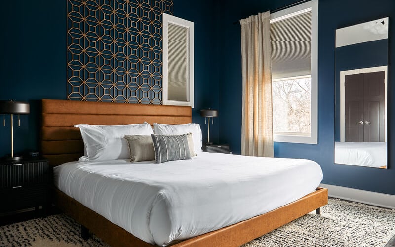 Modern bedroom with wood platform bed, white bedding, teal walls, and large window with beige curtains