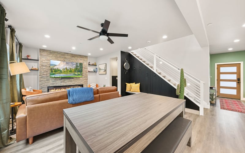 Open-plan living room with tan leather sofa, stone fireplace, ceiling fan, and pool table in foreground