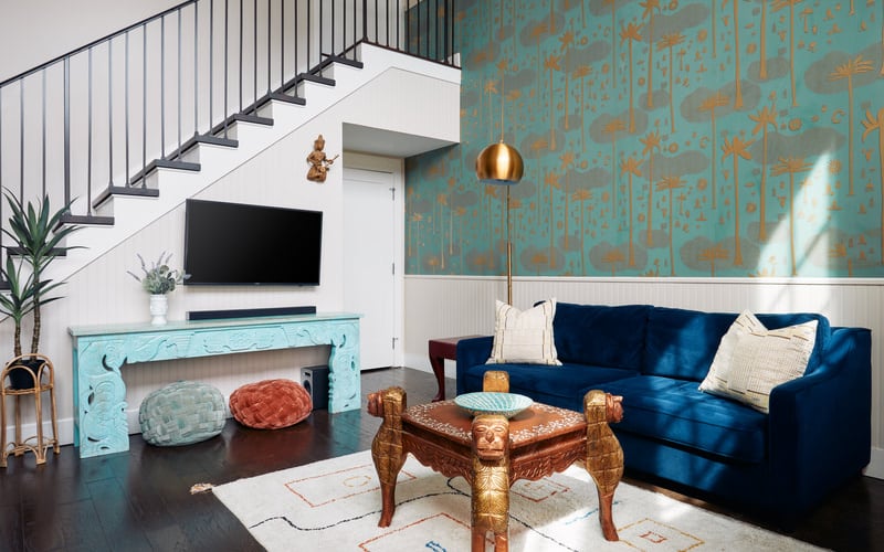 Modern living room with blue velvet sofa, turquoise patterned wallpaper, gold pendant light, and sculptural bronze coffee table