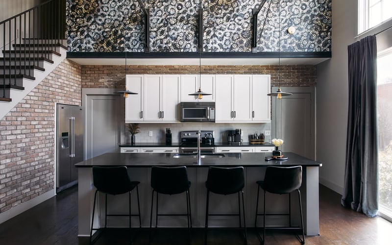 Modern kitchen with white cabinets, black island, stainless steel appliances, and exposed brick walls