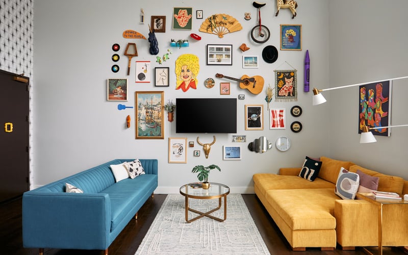 Living room with blue and mustard sofas facing gallery wall of eclectic art, vintage objects, and decorative items