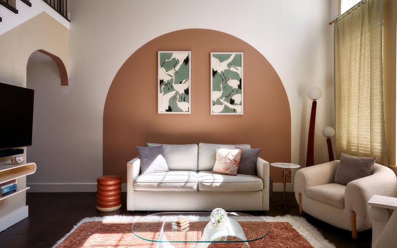 Modern living room with cream sofa, terracotta accent wall, botanical prints, and arched architectural details