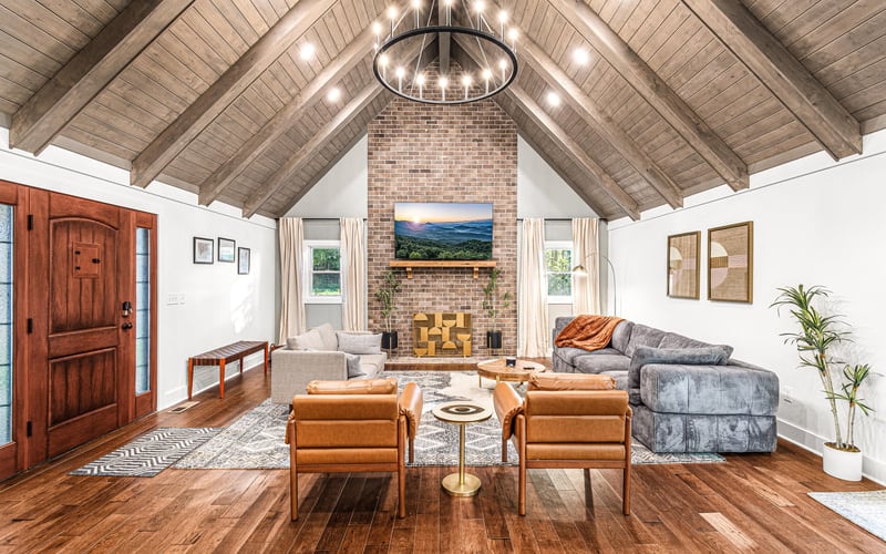 Vaulted living room with exposed wood beams, brick fireplace, leather chairs, and mountain landscape artwork