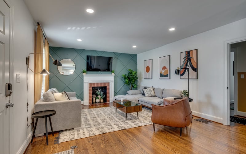 Modern living room with teal accent wall, fireplace, gray and brown seating, wood floors, and framed artwork