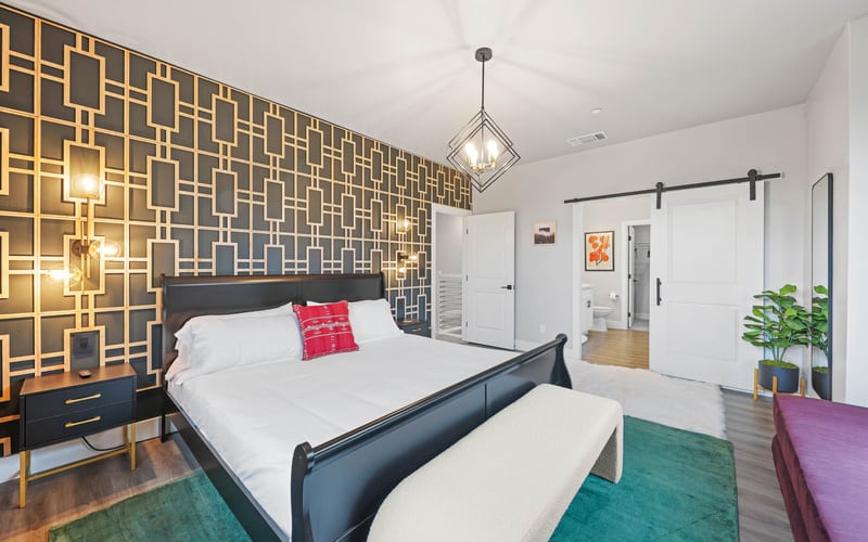 Modern bedroom with black metal bed, gold geometric accent wall, pendant light, and white barn doors