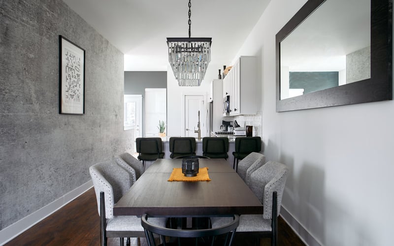 Dining room with dark wood table, gray upholstered chairs, crystal chandelier, and gray textured walls