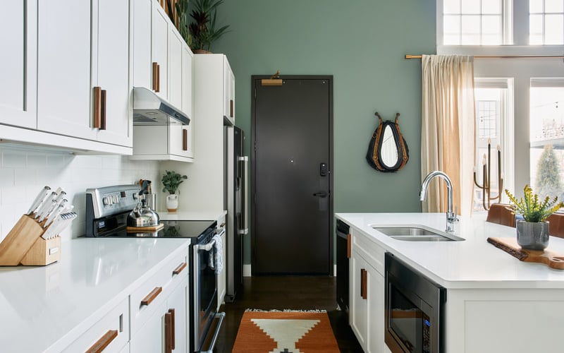 Modern kitchen with white cabinetry, sage green walls, black appliances, white countertops, and island with sink