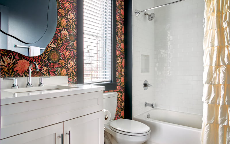 Modern bathroom with white vanity, floral patterned wallpaper, bathtub with shower, and city view through window