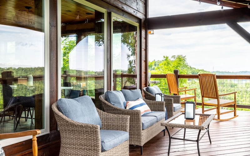 Covered deck with wicker seating, wooden chairs, and expansive views of green rolling hills and countryside
