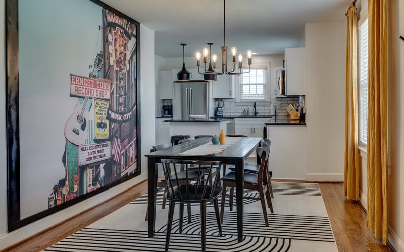 Dining area with black table and chairs, vintage record shop poster, open kitchen with stainless steel appliances, pendant lighting, and gold curtains.