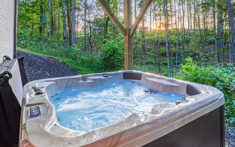 Hot tub with bubbling water on a covered deck overlooking dense forest at sunset