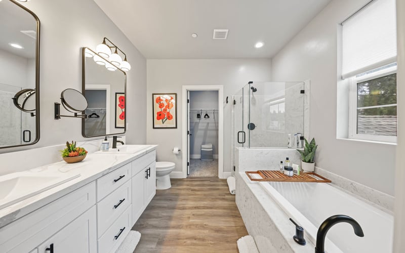 Modern primary bathroom with white vanity, dual sinks, freestanding tub, walk-in shower, and wood-look flooring