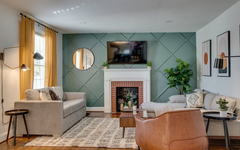 Living room with teal geometric accent wall, fireplace, TV, gray and tan seating, and yellow curtains