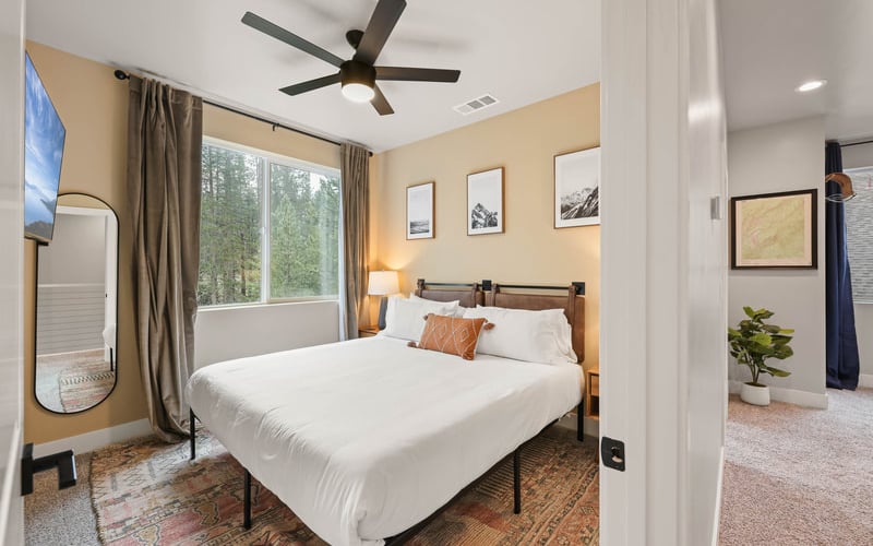 Bedroom with queen bed, yellow walls, ceiling fan, large windows with forest view, and adjoining bathroom