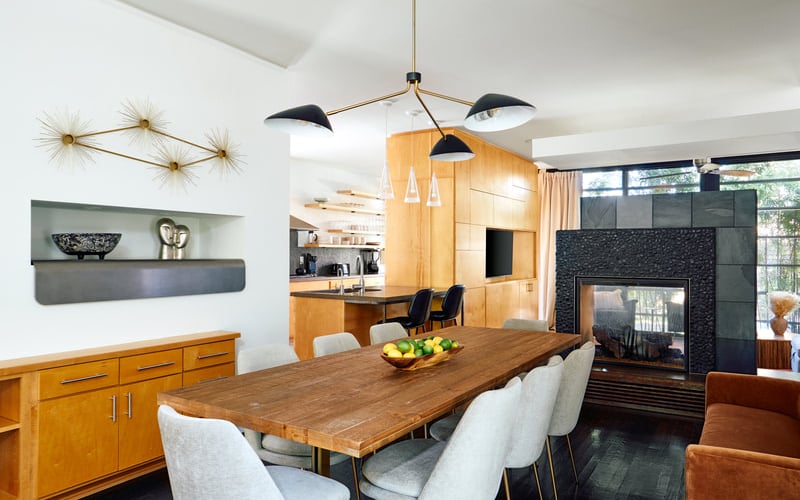 Open-plan dining and living room with wood table, fireplace, and modern pendant lighting