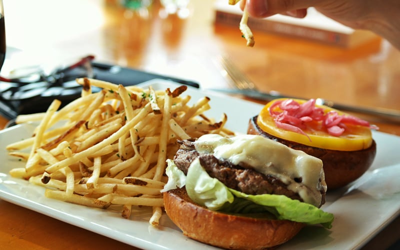 Cheeseburger with lettuce and melted cheese on toasted bun, served with crispy fries and open-faced sandwich with red toppings