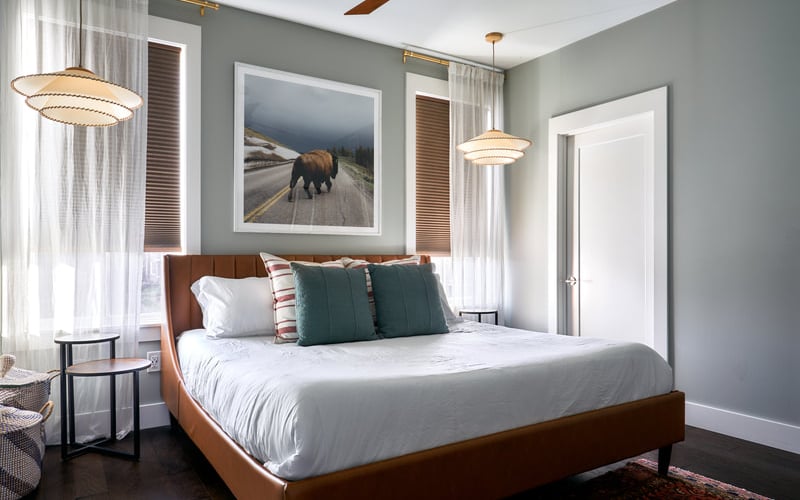 Bedroom with wood bed frame, white bedding, gray walls, pendant lights, and wildlife artwork above headboard