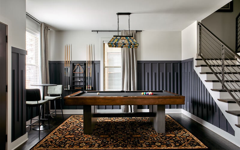 Game room with pool table, stained glass pendant light, black wainscoting, and staircase with metal railing