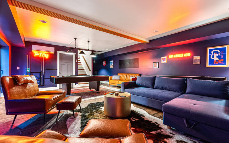 Basement game room with pool table, leather seating, neon signs, and colorful ambient lighting