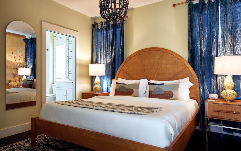Bedroom with wooden bed, rattan headboard, blue curtains, round mirror, and woven pendant light fixture