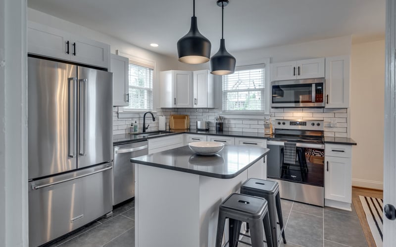 Modern kitchen with white cabinetry, stainless steel appliances, black pendant lights, and island with seating